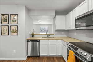 Kitchen featuring stainless steel appliances, white cabinetry, dark wood-style floors, and light stone countertops