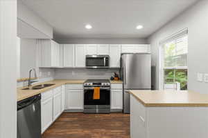 Kitchen with appliances with stainless steel finishes, white cabinetry, dark wood-style flooring, recessed lighting, and light stone counters