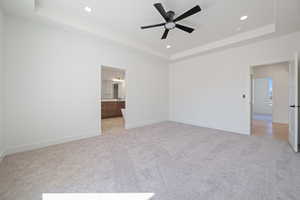 Unfurnished bedroom with a tray ceiling, ceiling fan, light colored carpet, connected bathroom, and recessed lighting
