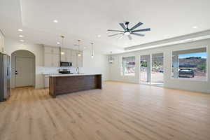Kitchen featuring open floor plan, a tray ceiling, pendant lighting, an island with sink, and stainless steel appliances