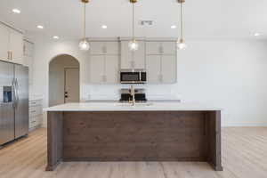 Kitchen with stainless steel appliances, an island with sink, arched walkways, recessed lighting, and hanging light fixtures