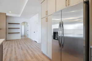 Kitchen with stainless steel fridge with ice dispenser, arched walkways, light wood-style floors, open shelves, and light countertops