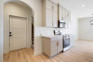 Kitchen with appliances with stainless steel finishes, light wood finished floors, arched walkways, recessed lighting, and hanging light fixtures