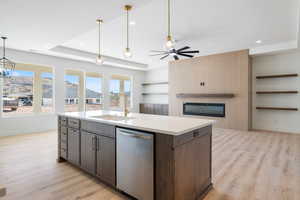Kitchen with stainless steel dishwasher, open floor plan, dark brown cabinets, an island with sink, and light wood finished floors