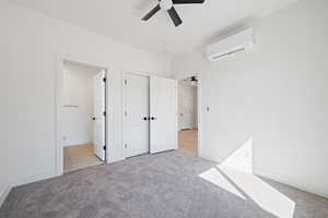 Unfurnished bedroom with light colored carpet, a wall unit AC, a ceiling fan, and connected bathroom