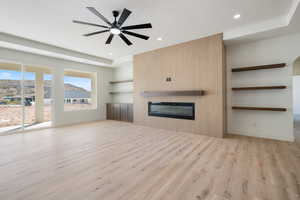 Unfurnished living room with light wood-style flooring, a glass covered fireplace, built in shelves, a ceiling fan, and recessed lighting