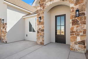 Entrance to property with stone siding, roof with shingles, and stucco siding