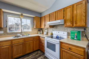 Kitchen featuring electric stove, brown cabinetry, light countertops, and under cabinet range hood