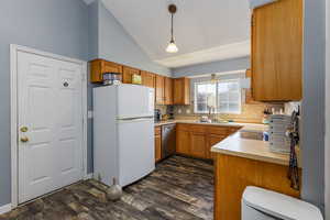 Kitchen featuring decorative light fixtures, brown cabinets, freestanding refrigerator, light countertops, and lofted ceiling