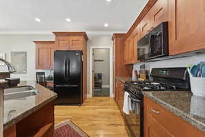 Kitchen featuring black appliances, brown cabinets, ornamental molding, light wood-type flooring, and recessed lighting