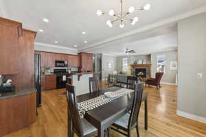 Dining space with crown molding, light wood-style floors, a warm lit fireplace, recessed lighting, and a chandelier
