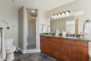 Full bathroom featuring double vanity, a shower stall, and stone tile flooring