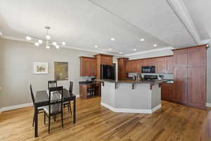 Kitchen featuring a breakfast bar area, brown cabinetry, dark stone counters, ornamental molding, and recessed lighting
