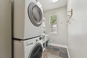 Laundry room featuring estacked washer and dryer and stone tile floors