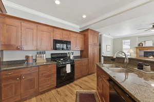 Kitchen featuring crown molding, black appliances, dark stone countertops, brown cabinets, and light wood-style flooring