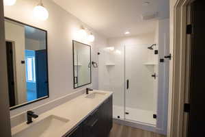 Full bathroom with a shower stall, double vanity, dark wood-style floors, and recessed lighting