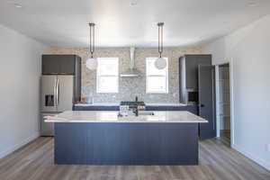 Kitchen with appliances with stainless steel finishes, a center island with sink, wall chimney exhaust hood, light wood finished floors, and recessed lighting