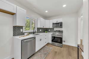 Kitchen featuring stainless steel appliances, white cabinetry, decorative backsplash, and recessed lighting
