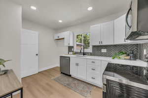 Kitchen with stainless steel appliances, white cabinetry, backsplash, recessed lighting, and light wood-style floors