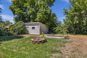 View of green lawn with a fire pit and an outdoor structure