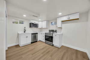 Kitchen featuring stainless steel appliances, white cabinets, light wood-type flooring, and recessed lighting