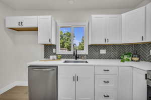 Kitchen with dishwasher, white cabinets, tasteful backsplash, wood finished floors, and light stone countertops