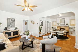 Living area with arched walkways, wood finished floors, a tiled fireplace, and ceiling fan