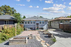 Rear view of house featuring a vegetable garden, a patio, a fenced backyard, and an outdoor fire pit