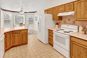 Kitchen with white appliances, light countertops, under cabinet range hood, backsplash, and ceiling fan