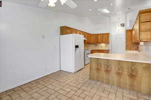 Kitchen with backsplash, white appliances, a peninsula, light countertops, and vaulted ceiling