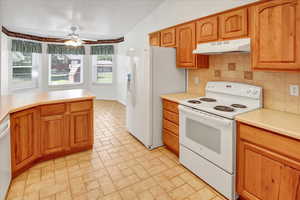 Kitchen featuring white appliances, light countertops, lofted ceiling, under cabinet range hood, and decorative backsplash