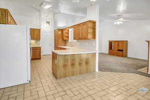 Kitchen featuring tasteful backsplash, freestanding refrigerator, light countertops, a peninsula, and a vaulted ceiling