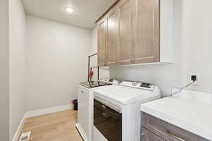 Main floor laundry room with cabinet space, light wood finished floors, and washer and clothes dryer