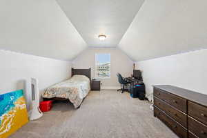 Bedroom featuring light colored carpet, lofted ceiling, a textured ceiling, and a desk