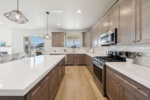 Kitchen with appliances with stainless steel finishes, decorative backsplash, pendant lighting, light LVP flooring, and light stone countertops