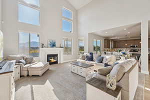 Living area featuring a glass covered fireplace, light colored carpet, high vaulted ceiling, and healthy amount of natural light