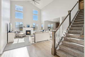 Living room featuring a glass covered fireplace, high vaulted ceiling, stairs, LVP floors, and ceiling fan