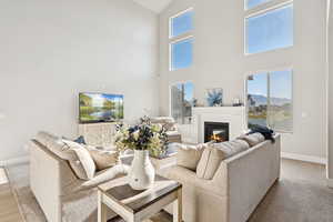 Living area featuring a glass covered fireplace, light colored carpet, and high vaulted ceiling