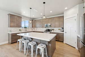 Kitchen with a breakfast bar area, tasteful backsplash, a center island, decorative light fixtures, and appliances with stainless steel finishes