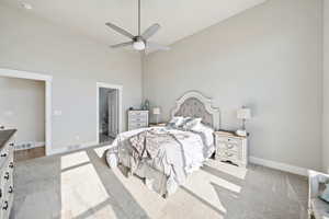 Primary suite with a towering ceiling, light colored carpet, ceiling fan, and connected bathroom