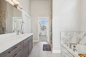 Bathroom featuring a garden tub, vanity, light tile patterned floors, and a towering ceiling
