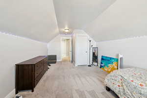 Bedroom with light carpet, lofted ceiling, and a textured ceiling