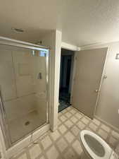 Bathroom featuring a shower stall, a textured ceiling, and light flooring