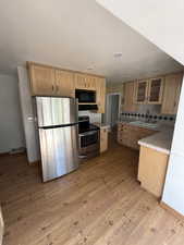 Kitchen with tile counters, stainless steel appliances, decorative backsplash, and light wood-style flooring