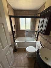 Bathroom featuring combined bath / shower with glass door, tile walls, light tile patterned floors, vanity, and a textured ceiling