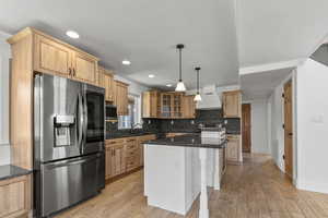 Kitchen featuring appliances with stainless steel finishes, tasteful backsplash, a center island, glass insert cabinets, and light wood-type flooring