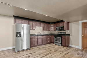 Kitchen with appliances with stainless steel finishes, a textured ceiling, light wood finished floors, and recessed lighting