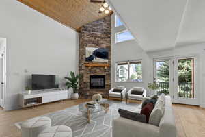 Staged living area with light wood-style flooring, high vaulted ceiling, wooden ceiling, and a stone fireplace