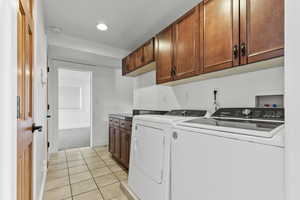Washroom featuring light tile patterned flooring, cabinet space, independent washer and dryer, and light colored carpet