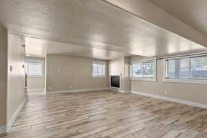 Unfurnished living room with a textured ceiling, light wood-style floors, and a glass covered fireplace